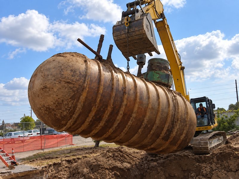 An excavator lifting a corroded underground fuel tank out of the ground
